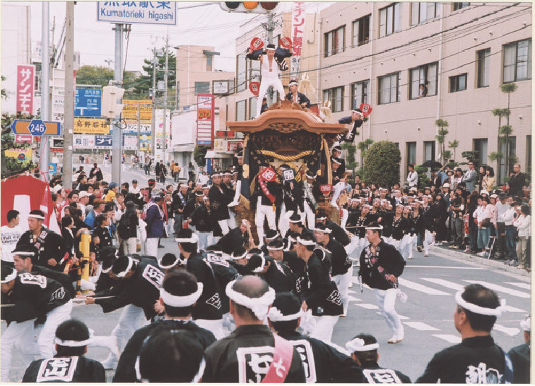 道路信号の下を通る七山地車をたくさんの人達が引いている写真