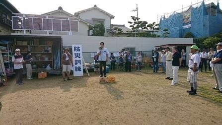 広場で拡声器を持ち話す町長と話を聞く参加者の写真