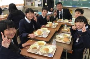 北小学校の6年生と一緒に給食の席について、笑顔でピースサインをする町長の写真