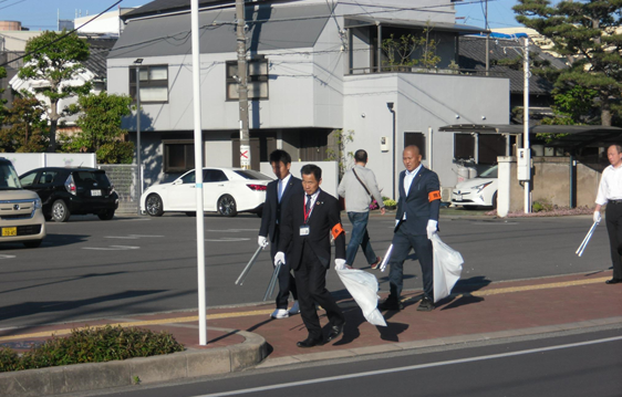 歩道の上を手に袋と火ばさみを持ちゴミ拾いをする町長の写真