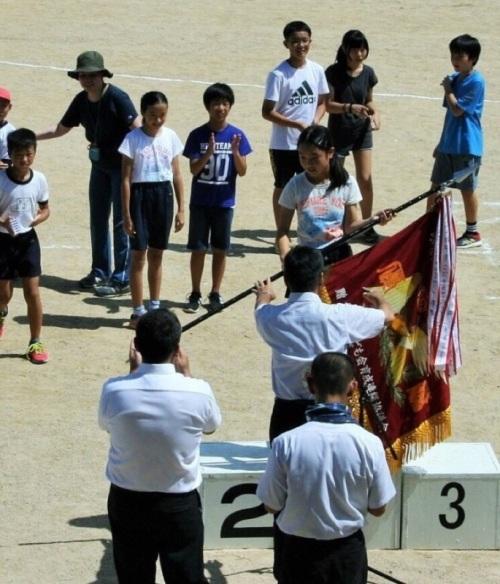 表彰台の上に立つ女の子が優勝旗を手渡されている写真