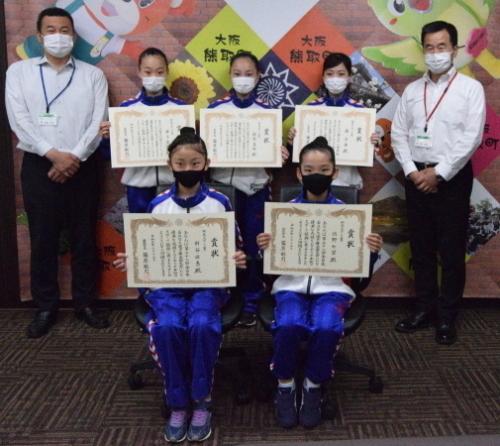 町長と白いシャツ姿の男性、賞状を持ったジャージ姿の女子生徒5名が写っている写真