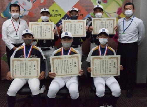 町長と白いシャツ姿の男性、賞状を持った野球のユニフォーム姿の6名の学生たちが写っている写真