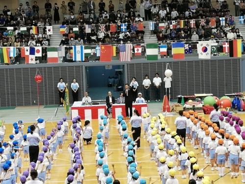 黄色や水色などのカラー帽子を被った幼稚園児たちが縦に並んで、町長の話を聞いている写真