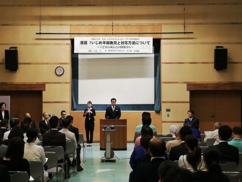 中央の演台で話をする町長、横には手話をする女性、出席者たちが椅子に座り話を聞いている写真