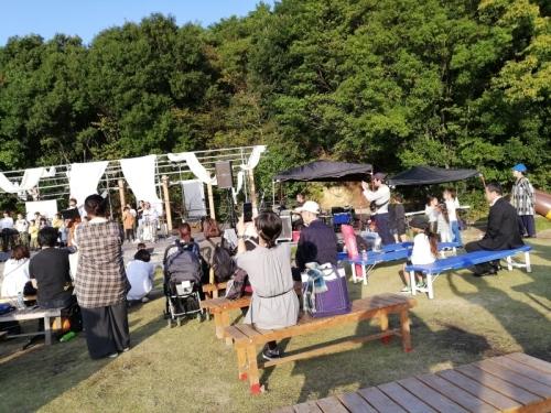 舞台上でギータを持った女性のライブが行われており、ライブを観覧する人たちを後ろから写している写真