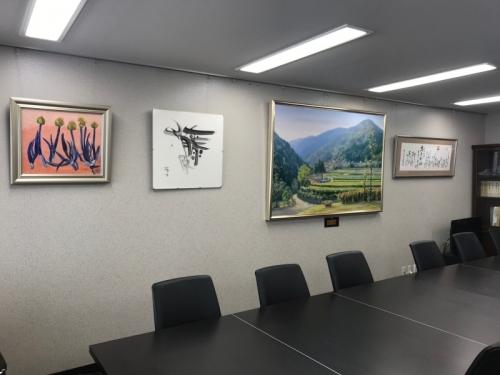 机といすが置かれた室内の壁に書道の作品や絵画が4点飾られている写真