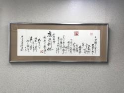 横長の額縁に入っていて、文字が沢山書かれている書道の作品が壁に飾られている写真