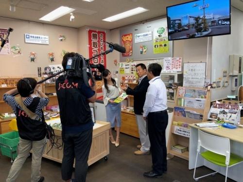 カメラの前で立ちながら話すアナウンサーと町長と町長の写真