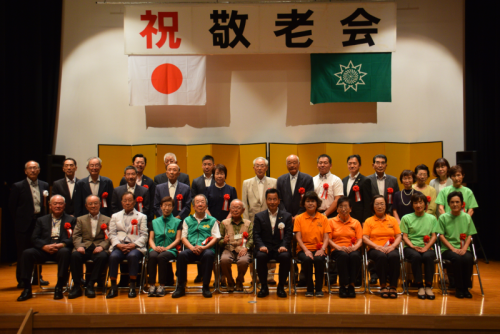 金屏風を背に笑顔で映る敬老会に参加した方々の集合写真