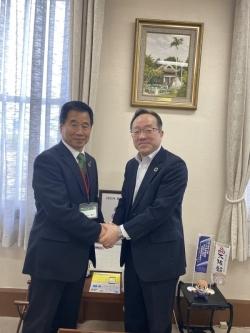 町長と山野副知事が横並びでお互いの両手を重ねて握手をしている写真