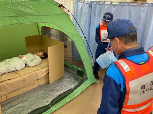 テント内の段ボールベッドに横たわる人