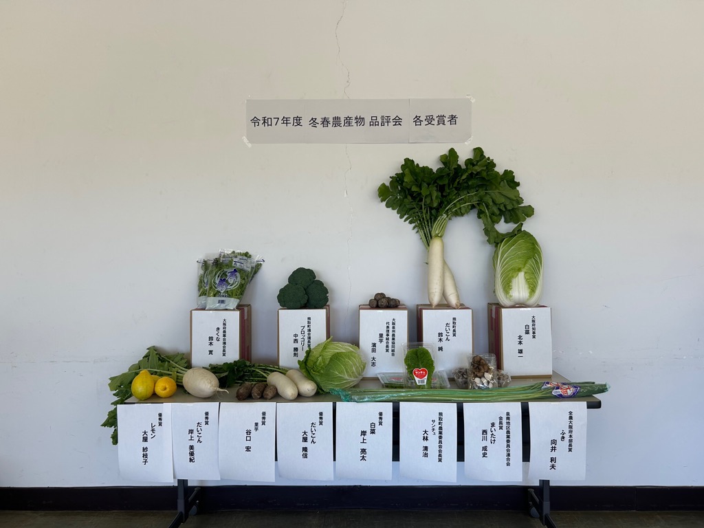 令和7年冬春農産物品評会にて受賞した方の氏名が書かれた紙とその上に受賞した各種野菜が載っている写真