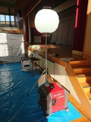 体育館のステージの下に敷かれたブルーシートの上に設置されたLEDで光っているバルーンライトの写真