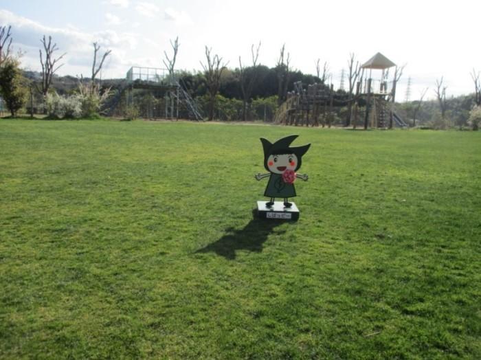 芝生の張られたサブグラウンドに葉っぱが描かれた緑色のスカートを着たキャラクターが立っている写真