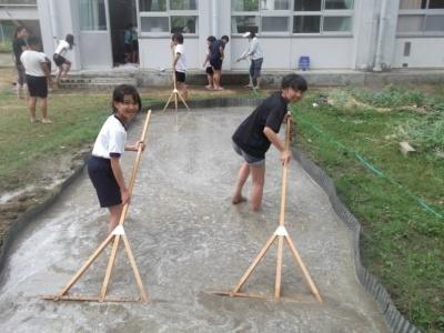 校内の敷地に作られた田んぼの水の中で女子生徒2人がトンボを引いている写真