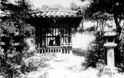 石灯籠の奥に設置された、お堂の中に保管されている石造地蔵菩薩立像の白黒写真