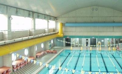 中央に縦長のコースがあるプール、横には赤の水深調整台が置かれている室内プールの写真