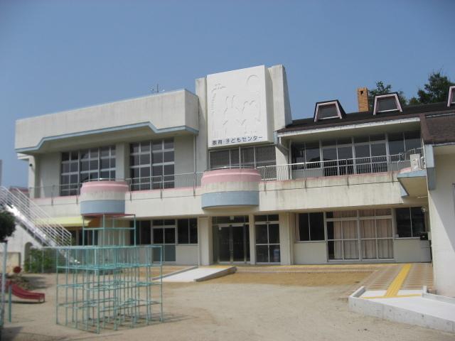 白い外壁で2階建ての教育・子どもセンターの建物、広い園庭、ジャングルジムの写真