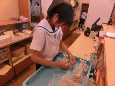 一人の女子生徒が、職場体験先で青いかごの中で袋詰めの作業をしている様子の写真