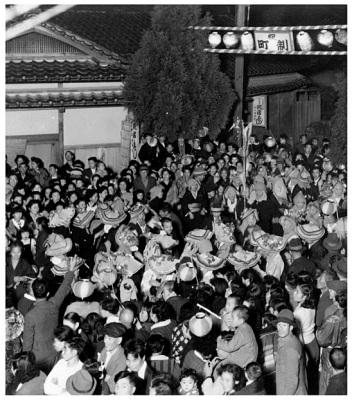 祝町制と書かれた紅白の門の下で、花笠や紅白提灯を手に持ちお祝いをするたくさんの人々の白黒写真