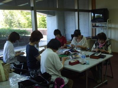 2つの長机をつけて3名ずつ向かい合って座り、布絵本作りを行っているいちごの会の活動の様子の写真