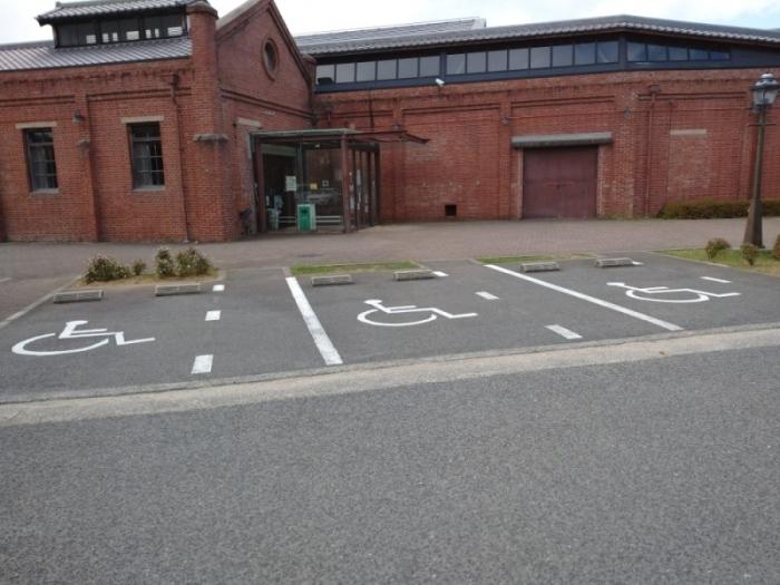 赤レンガ造りの建物の前に、3箇所の車いす使用者用駐車区画の駐車場が整備されている写真