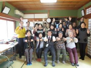 参加者達が3列に横並びに並んでいて、中央に町長のいる前列は両手でグー、真ん中の列の人達はチョキ、後ろの列の人達はパーをしている写真