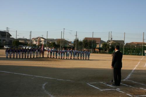グラウンド場で野球のユニフォーム姿の子供たちが横一列に並んでいて、子供たちの前で町長が話をしている写真