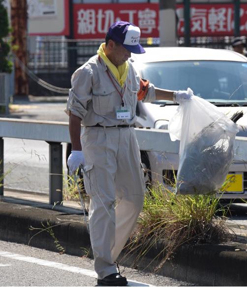 道路脇でゴミ袋と火ばさみを手にゴミ拾いをする男性職員の写真