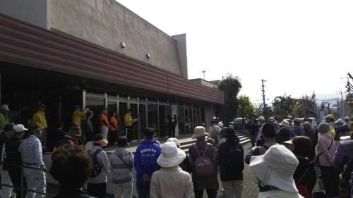 手前には歩こう会の参加者たちが並んでいて、奥には建物の前に立ち参加者に向かって話をする町長が写っている写真