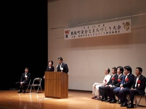 頭上に熊取町安全なまちづくり大会と幕がかけられた舞台上で町長が話をしている写真