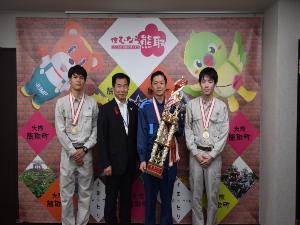 メダルを首にかけ、トロフィーを持った男性3名と、町長の記念写真