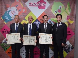 ジャンプ君とメジーナちゃんのが描かれた壁の前で感謝状を持った岸本氏、山下氏、木下氏、町長が並んでいる記念写真
