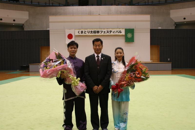 体操のフロアマットの上で町長と花束を持った陳老師、渡邊老師が並んでいる記念写真
