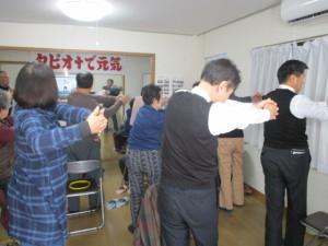 両手を合わせ伸ばす体操をする男女の写真