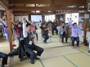 町長と参加者達が椅子に座って右手を上げて体操をしている写真