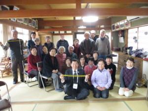 畳の部屋で最前列に紐を持った町長が座っていて、後ろに参加者達が集まっている写真