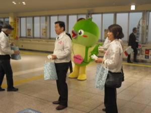 熊取駅改札前で啓発活動を行っている町長とメジーナちゃんの写真