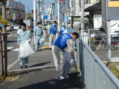 作業着姿の男性、青いビブスをつけた女性や男性達がゴミ袋や火ばさみを手に持ち道路の清掃をしている写真