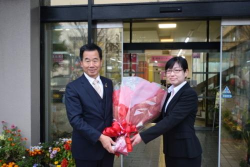 町長がスーツ姿の女性から花束を渡されほほ笑んでいる写真