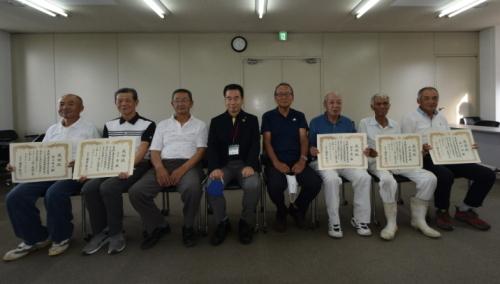 中央に町長が座り、左端から2名、右端から3名の男性が賞状を持って座っている記念写真