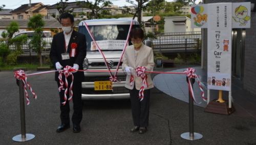 手前には紅白のテープをカットする町長と白いジャケット姿の女性、奥には車が置かれている写真