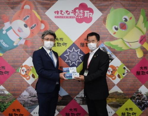 西村拓憲理事長が町長にマスクの箱2箱を手渡している写真
