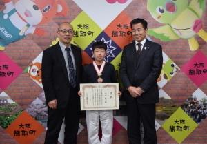 メダルをかけ、賞状を持つ清原維人さんと、左右に立つ町長と男性の記念写真