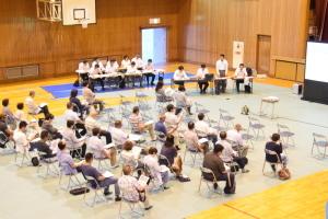 体育館で、パイプ椅子に座り話を聞いている住民の写真