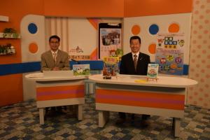 テレビ局のスタジオ内でアナウンサーの男性と町長が笑顔で座っている写真