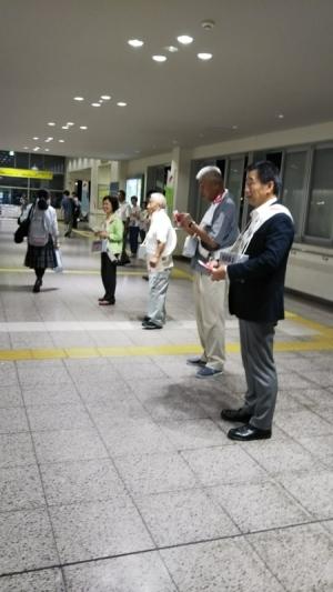 タスキをかけた町長や関係者たちが駅の構内で赤い羽根を持って立っている写真
