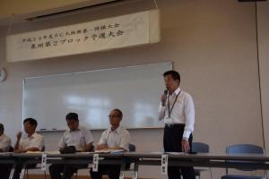 横一列に配置された席に座っている関係者と、マイクをもって話をしている町長の写真