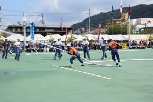 作業着姿の消防団員が長いホースを両手に持ち放水している様子を写している写真